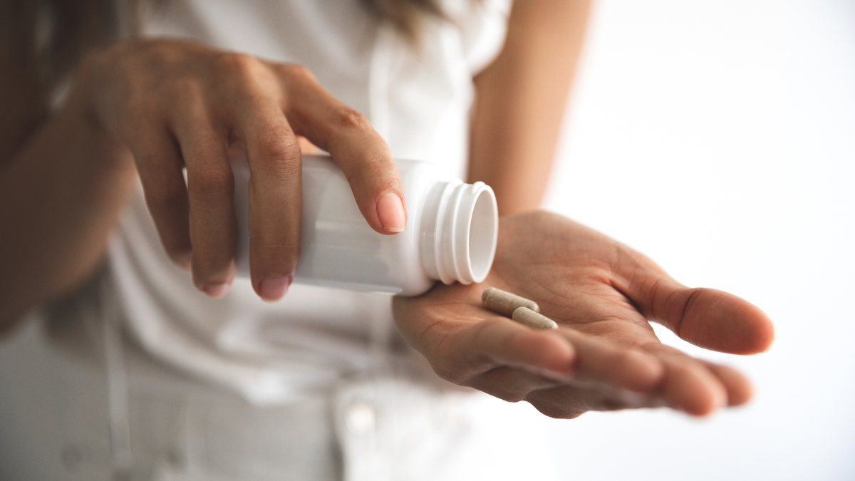 a woman pours supplements for alcohol withdrawal and cravings into her hand out of a white bottle