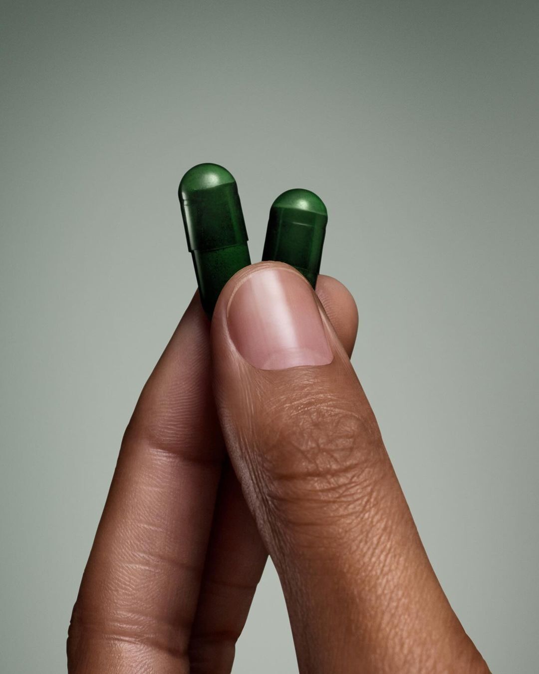 Hand holding two green capsules against a gray background